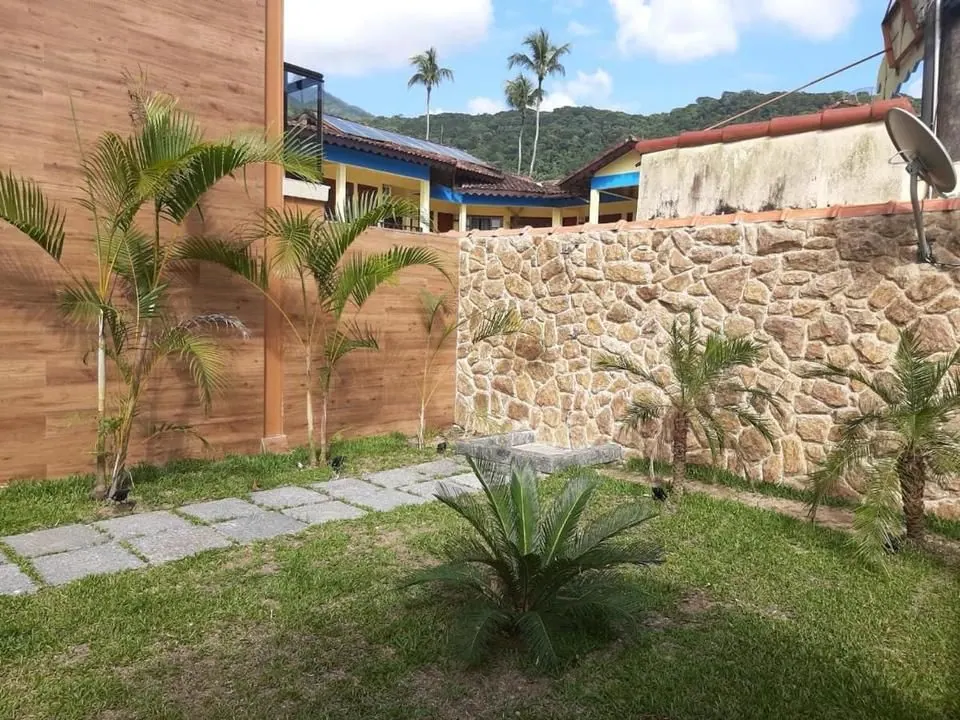 Jardim gramado do Bugio Flats com caminho de pedras, palmeiras e muro de pedra, com o morro ao fundo